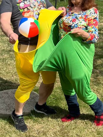 Two people outdoors wearing colorful inflatable pants, playing with a beach ball