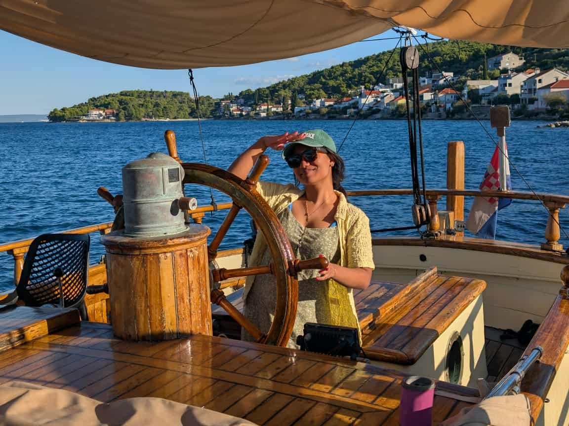 The writer steering a wheel on a boat in Croatia, with the water in the background.