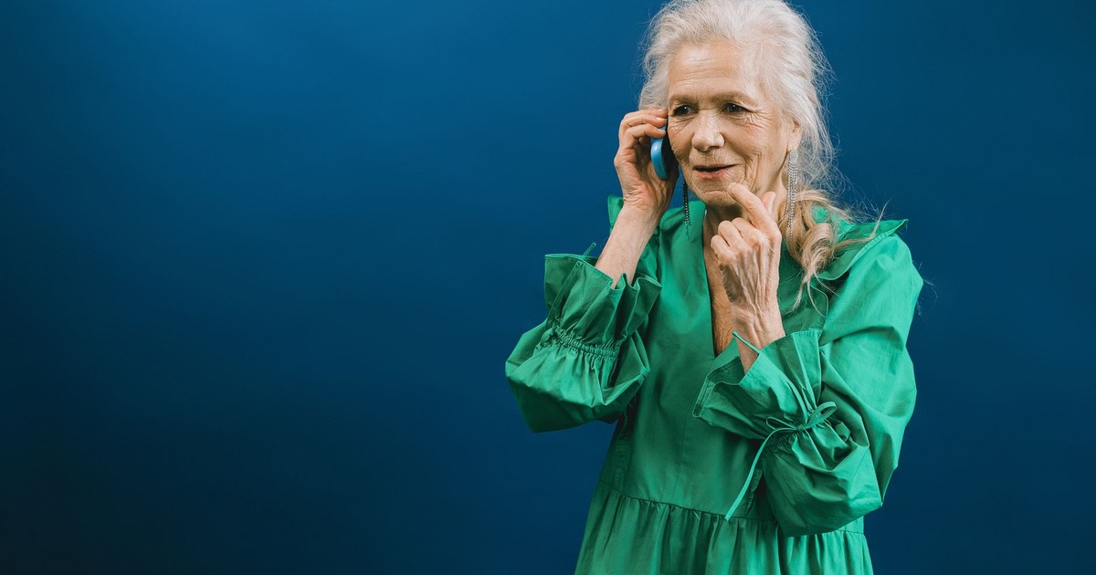 Senior woman in green dress talking on a mobile phone against a blue background.