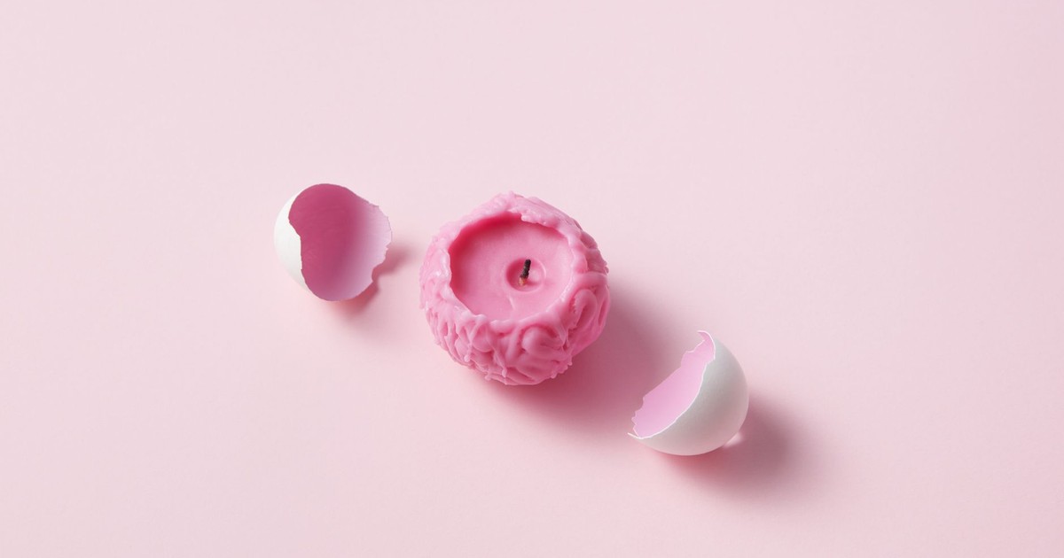 A unique pink candle shaped like a brain surrounded by white eggshells on a light pink background.