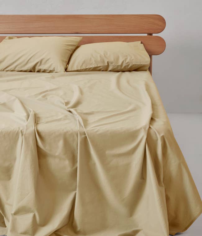 Minimalist bed with light sheets and wooden headboard, showcasing a simple and elegant bedroom style
