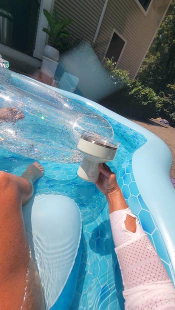Person relaxing on an inflatable pool float, holding cup