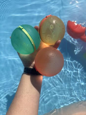 Hand holding three water balloons over a pool