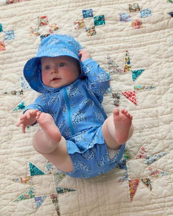 Baby in a hooded, turtle-patterned outfit lies on a quilt