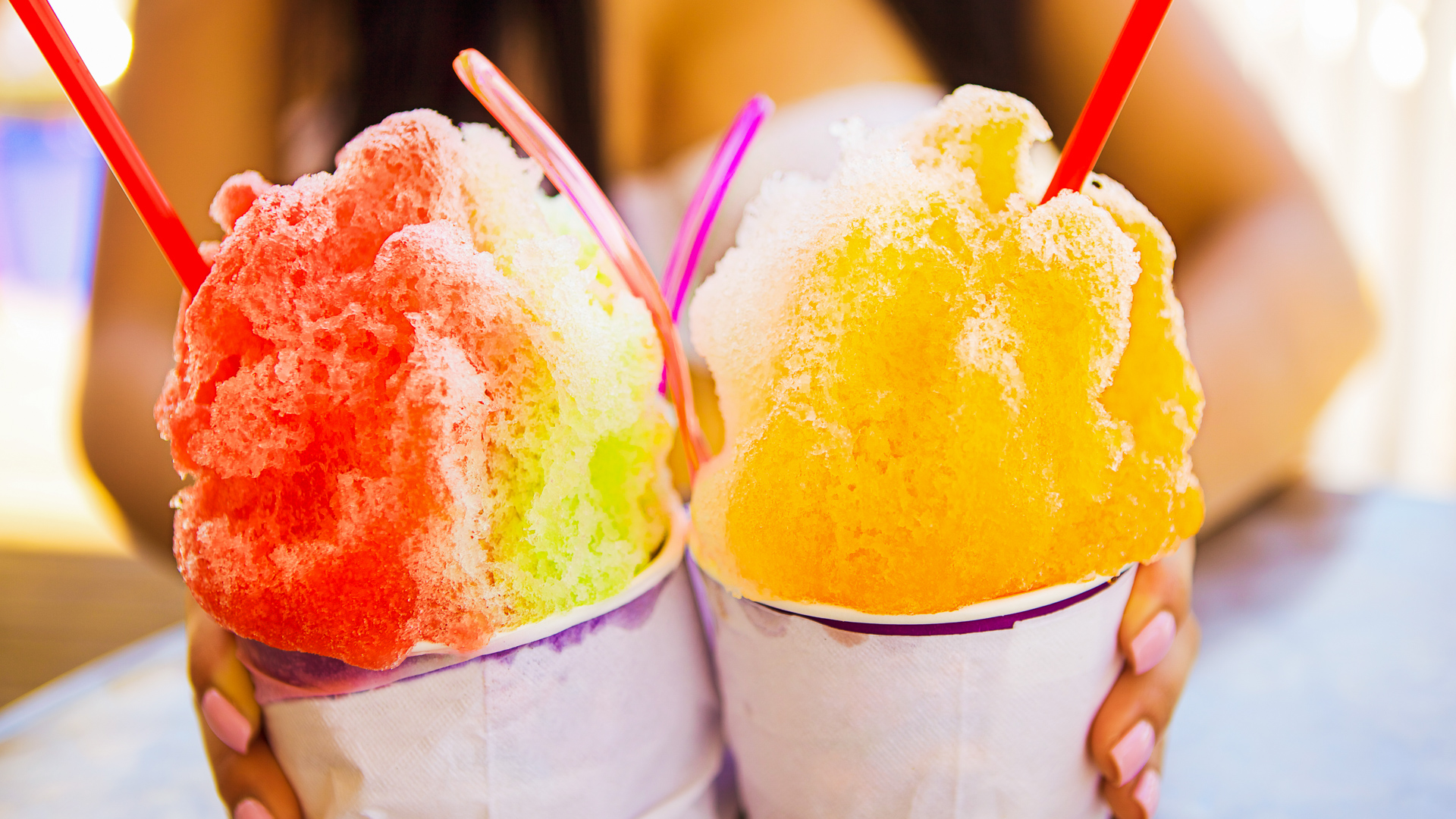 Discover a young girl holds two cups in front of her containing colorful arrangements of shaved ice