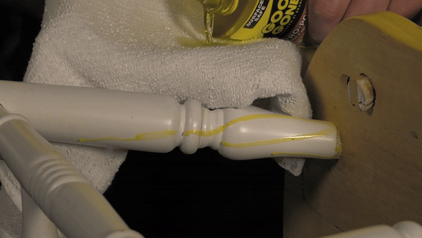 Close-up of a person's hand applying Goo Gone to a wooden chair to remove dried up glue