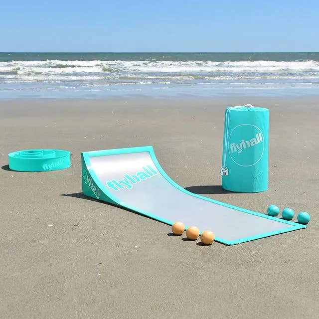 Flyball beach game set with ramp, balls, and carrying case on sand by the ocean
