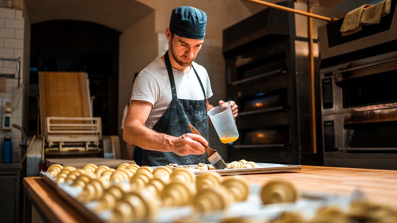 A pastry chef brushes pastry with egg.