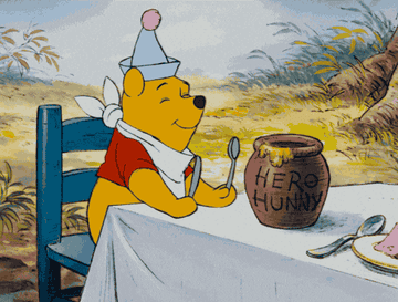Winnie the Pooh wearing a party hat, sitting at a dining table with a jar of honey in front of him