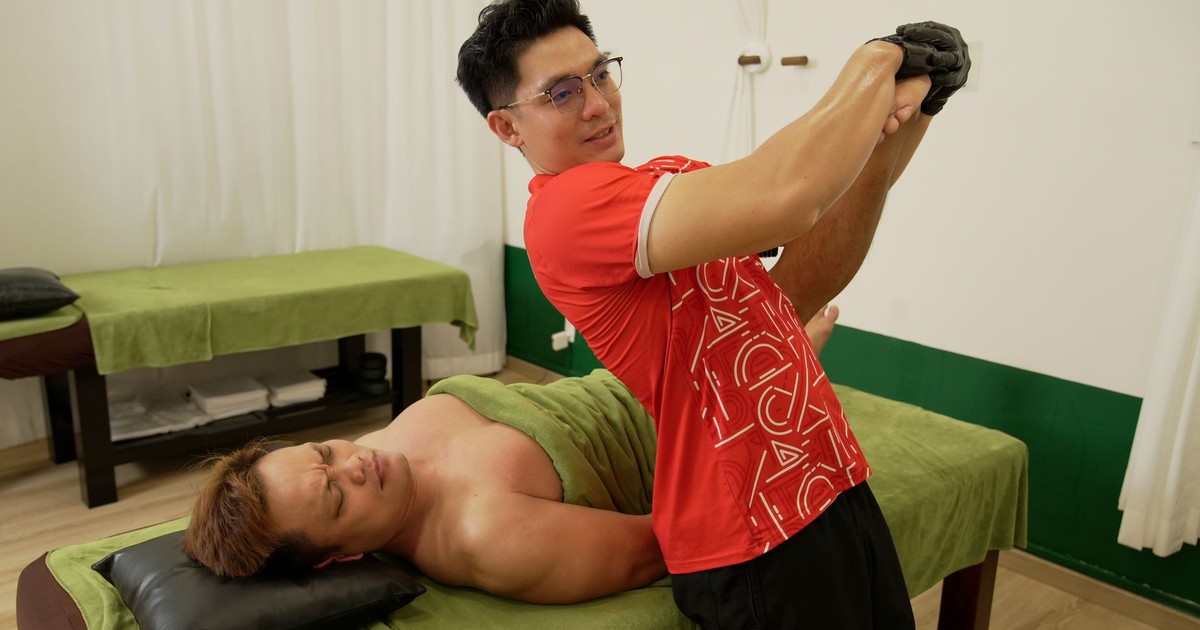 A therapist is performing stretching therapy on a patient in a clinic setting, focusing on arm and shoulder mobility.