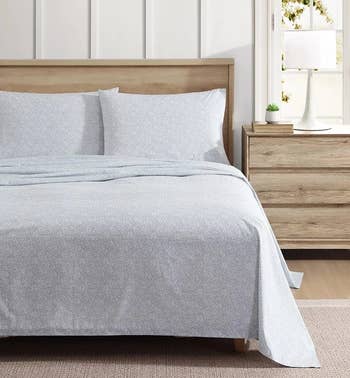 Cozy bedroom with a bed featuring a textured duvet and pillow set, wooden headboard, bedside table with lamp and small plant