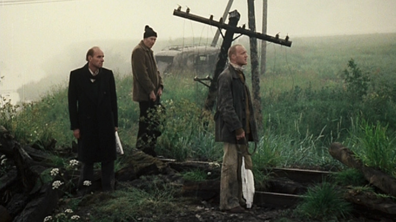 Stalker (Alexander Kaidanovsky) and the writer (Anatoly Solonitsyn) survey a grassy field while the professor (Nikolai Grinko) sits nearby in Stalker (1979)