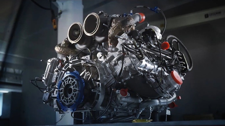 A compact twin-turbo V6 racing engine sitting on a bench in a dimly lit workshop.