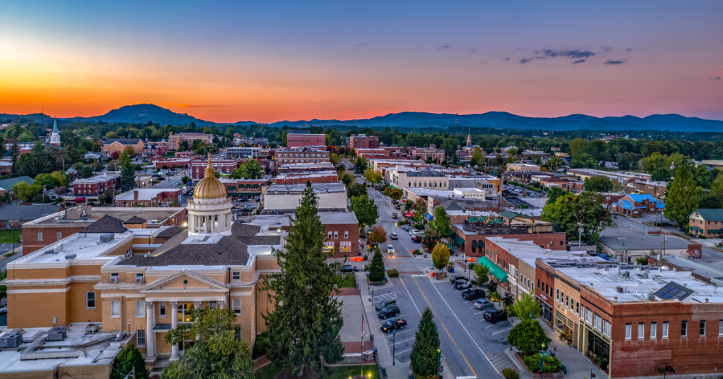 An aerial view of downtown Hendersonville, North Carolina, featuring historic brick buildings, tree-lined streets, and cars parked along Main Street.