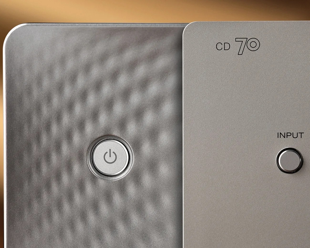 Close-up of a silver device with a textured power button and a smooth input button labeled "CD 70".