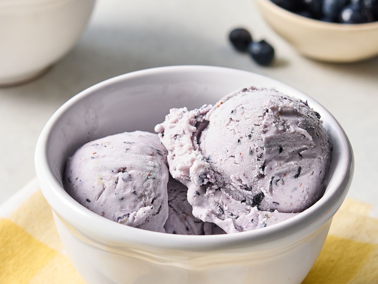 Two scoops of blueberry ice cream in a white bowl on a table