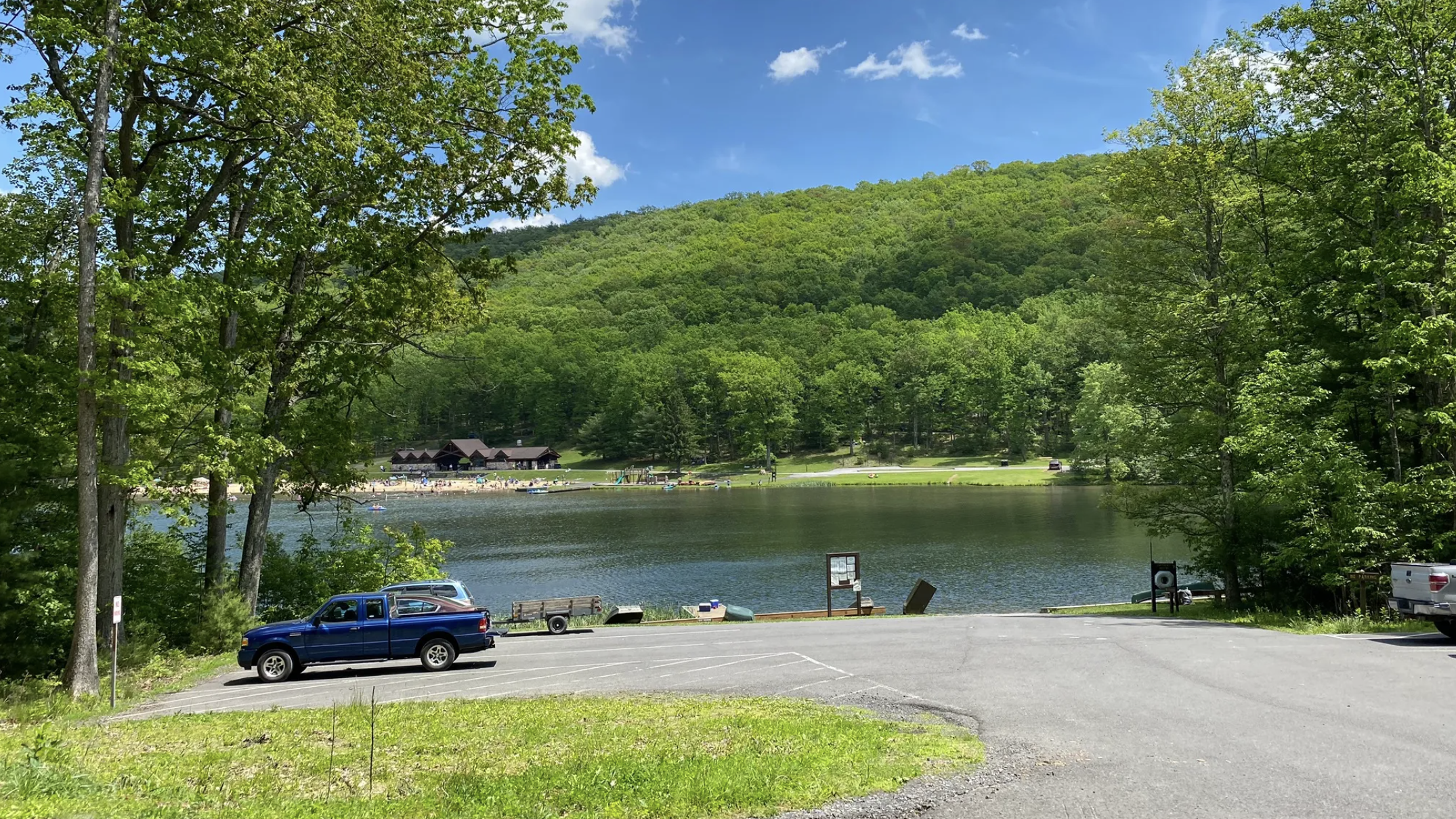 A parking lot near the water with a beach on the other side of the lake.