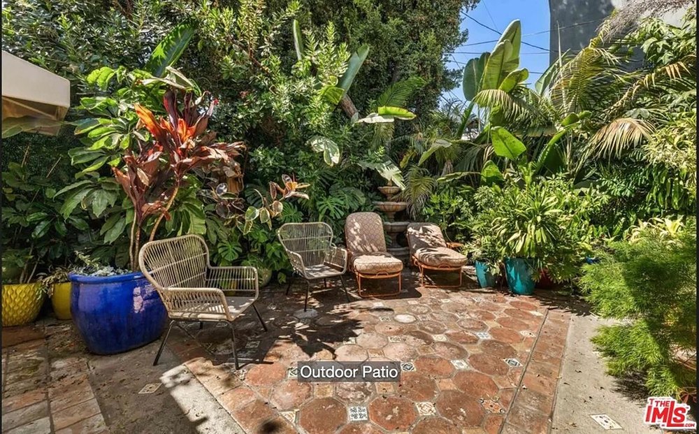 Charming terracotta tiled outdoor patio surrounded by lush tropical landscaping and wicker seating.