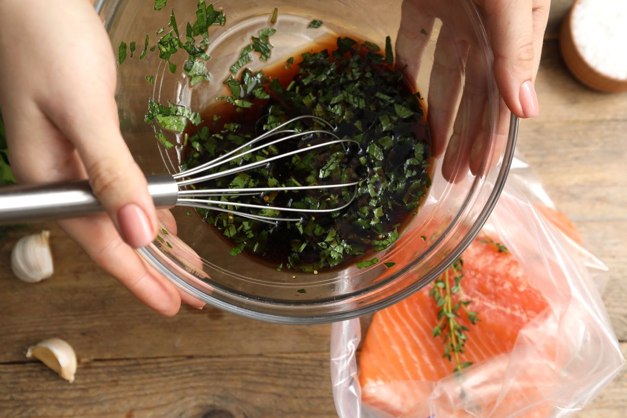 A person whisking herbs and sauce in a bowl near raw salmon