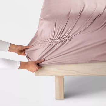 person stretching fitted sheet onto bed