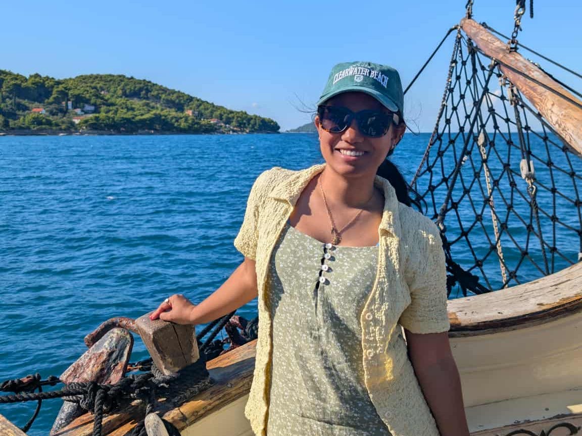 The writer wearing a dress and a hat, standing on a boat in front of the sea in Croatia.