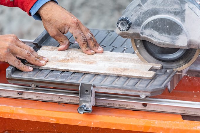 Worker Using Wet Tile Saw To Cut Wall Tile At Construction Site