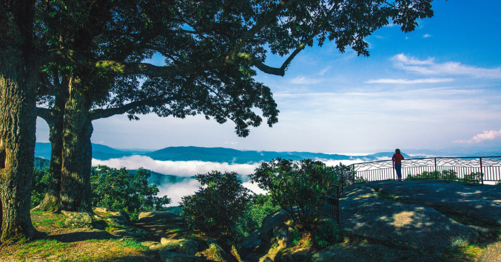 A panoramic scenic overlook from Jump Off Rock showing layers of the Blue Ridge Mountains stretching into the distance under a clear sky.