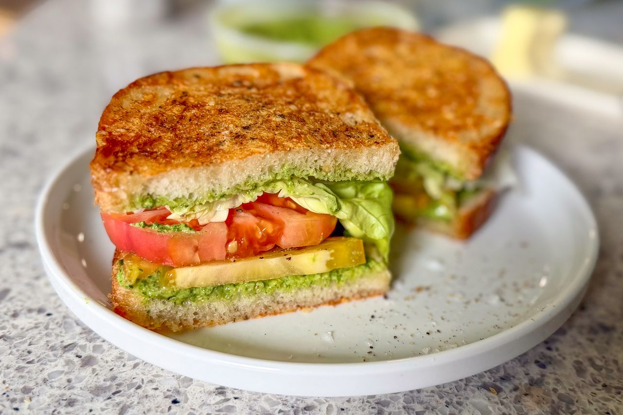 A sandwich featuring sliced tomatoes lettuce and other ingredients served on a white plate