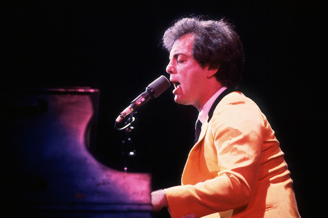 Billy Joel performing while seated at a piano singing into a microphone