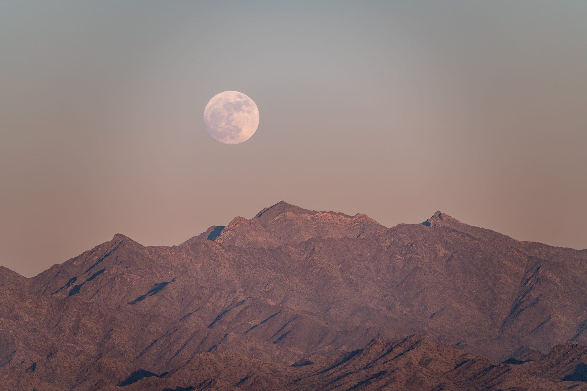 The near-full moon rises over the Estrella Mountains at sunset on June 28, 2026.