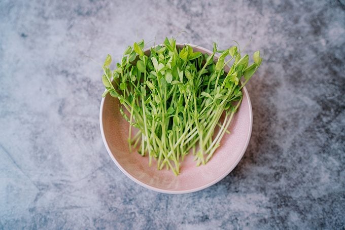 Green Pea Microgreens Lie In A Deep Pink Plate On A Marble Table. Top View