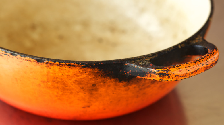 Closeup image of a well-used orange Le Creuset pot, with the exterior showing extensive blackening around the handles and rim, and the interior badly discolored