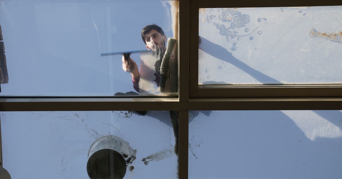A male window cleaner washing the exterior glass roof from above with a tool during daylight.