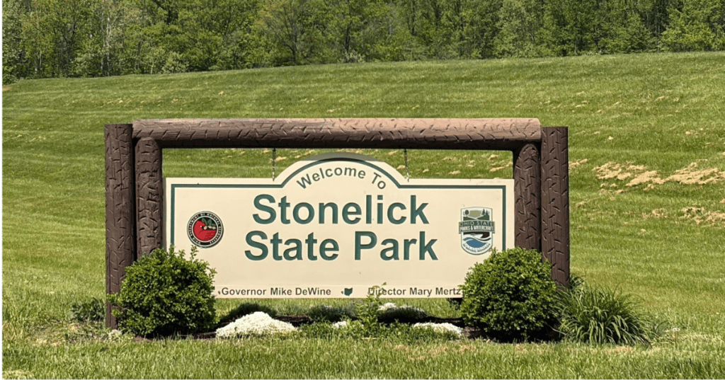 The official wooden welcome sign for Stonelick State Park in Ohio surrounded by green grass.