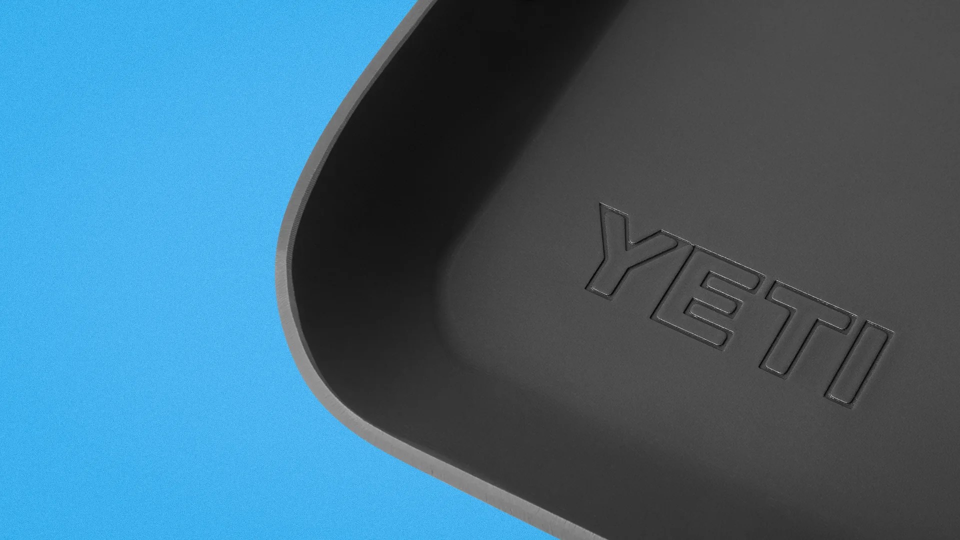 Close-up of a black YETI branded container corner on a blue background.