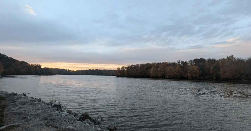 Calm autumn sunset over Stonelick Lake in Ohio with colorful fall foliage lining the shoreline.