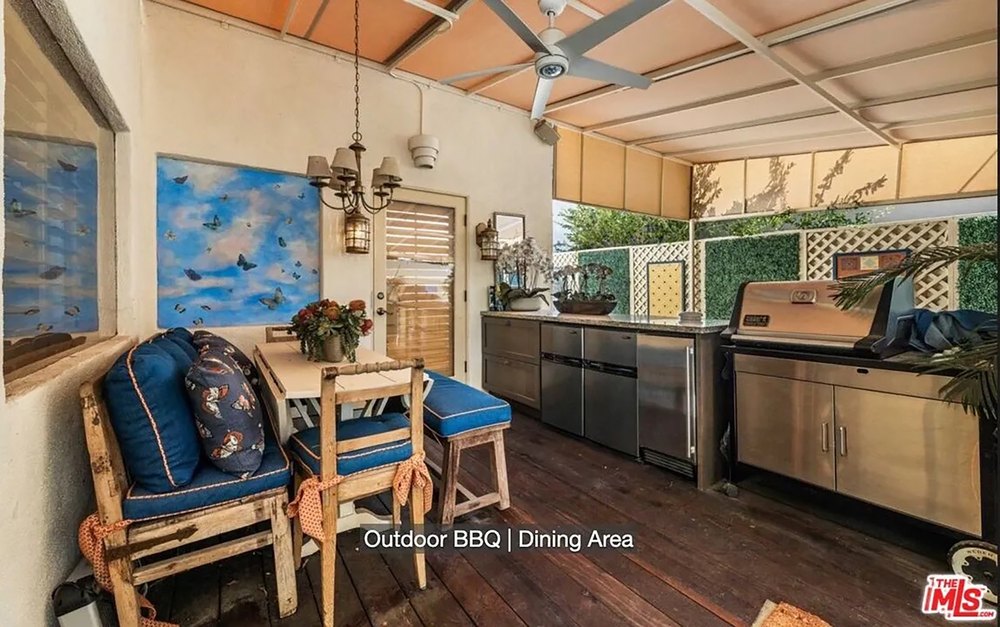 Covered outdoor kitchen and dining area featuring a stainless steel grill and blue-cushioned benches.