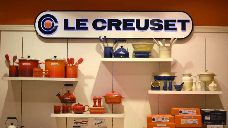 Retail display of Le Creuset products in different color schemes, beneath a large sign bearing the brand name
