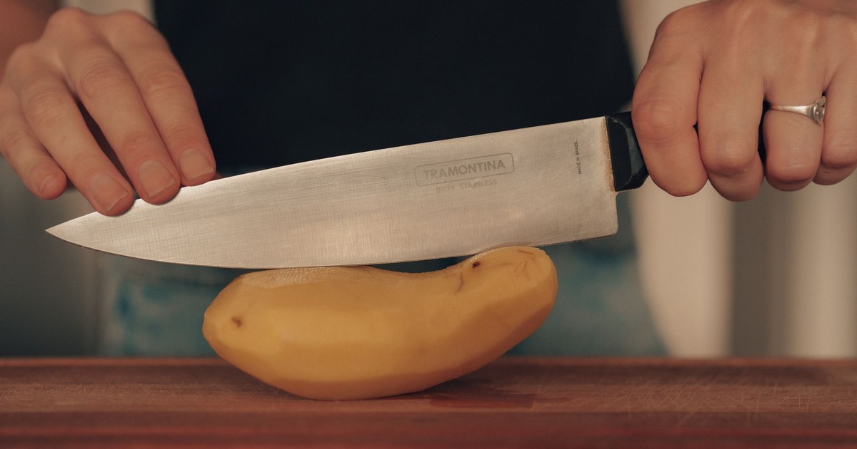 Close-up of hands slicing a potato with a kitchen knife, emphasizing cooking preparation.
