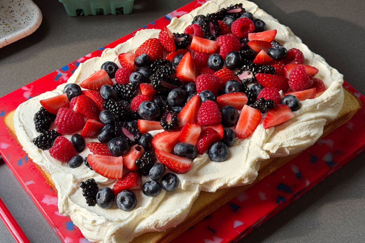 A rectangular cake topped with whipped cream and various fresh berries