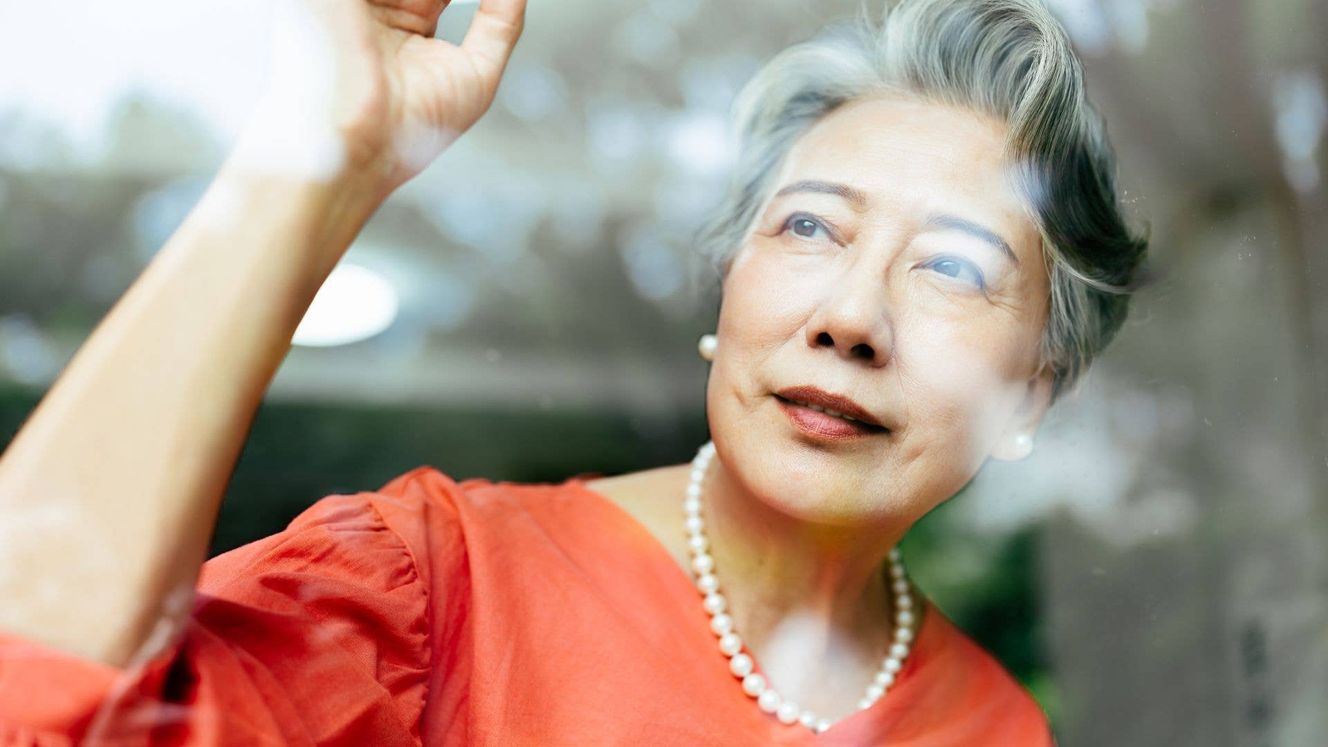 Close up of elegant Asian elderly woman looking through window at home.