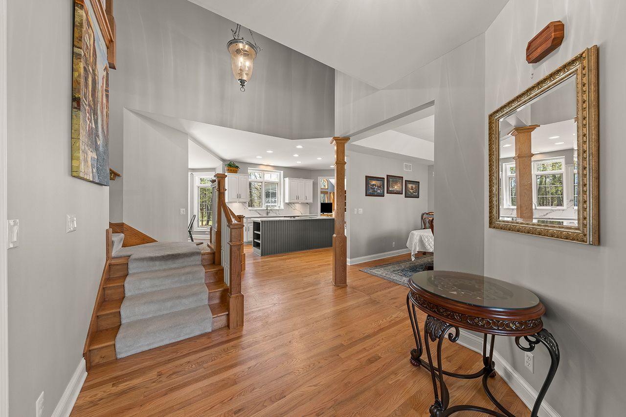 An interior view of a house entryway with wooden floors stairs a dining area on the right and a kitchen visible in the background