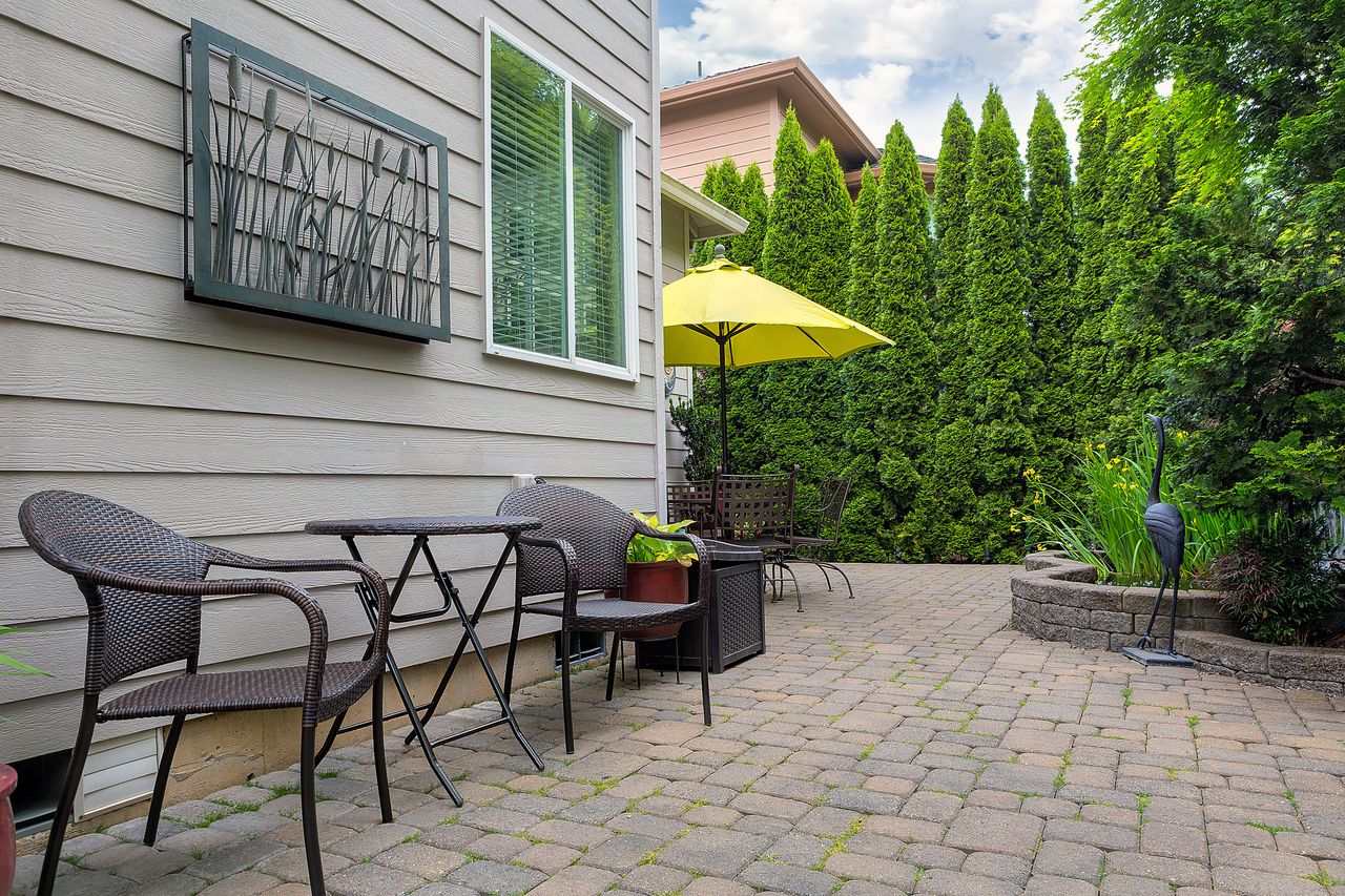 Outdoor patio area with a table chairs and a yellow umbrella surrounded by trees and greenery