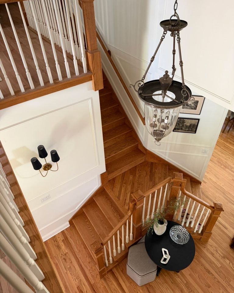 A wooden stairway with a chandelier and a small round table positioned below captured from an elevated perspective