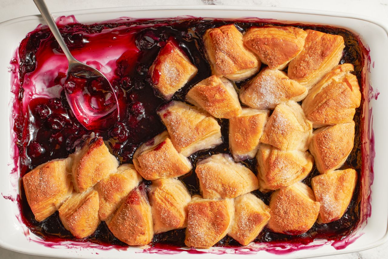 A blueberry cobbler with biscuit topping in a baking dish a spoon resting on the side