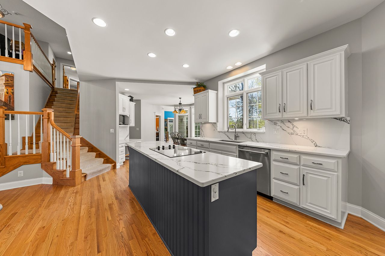 A modern kitchen featuring a central island marble countertops and a staircase in the background