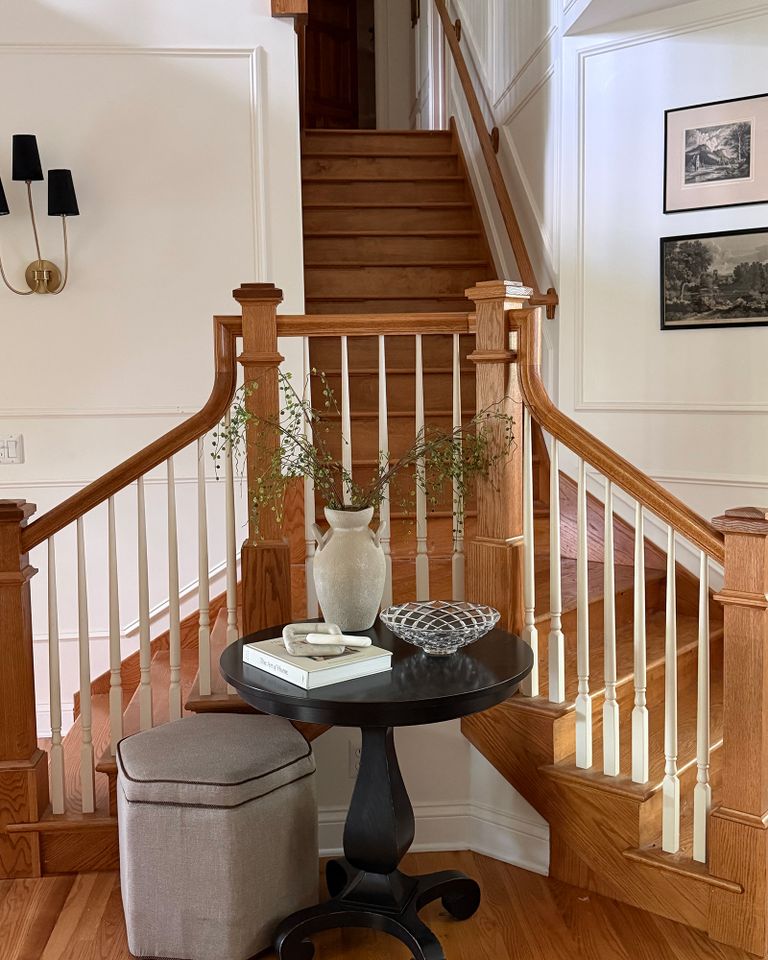 A staircase with a small round table and decorative items placed in front of it framed by wooden railings with white spindles