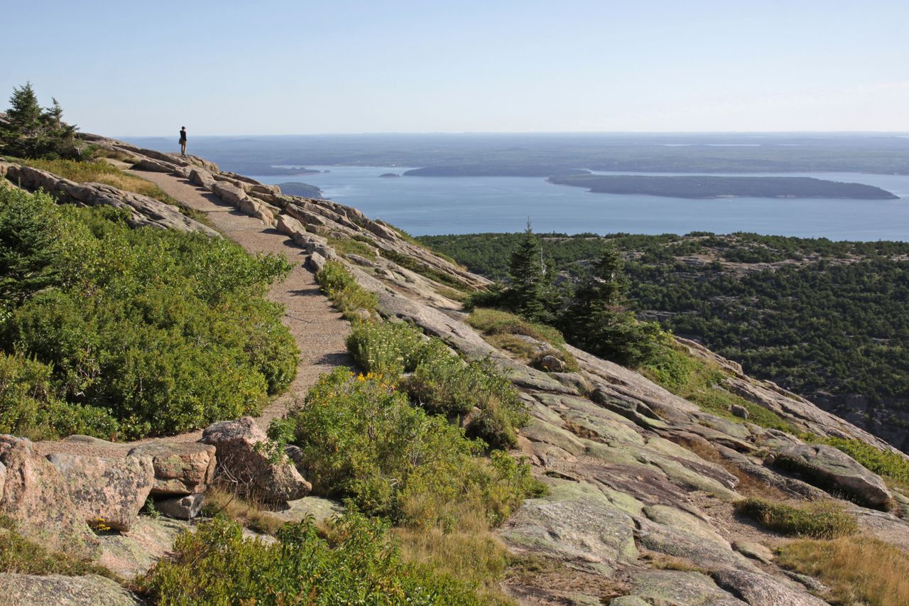 A scenic view from a rocky mountain trail overlooking distant islands and water a person stands on the trail to the left