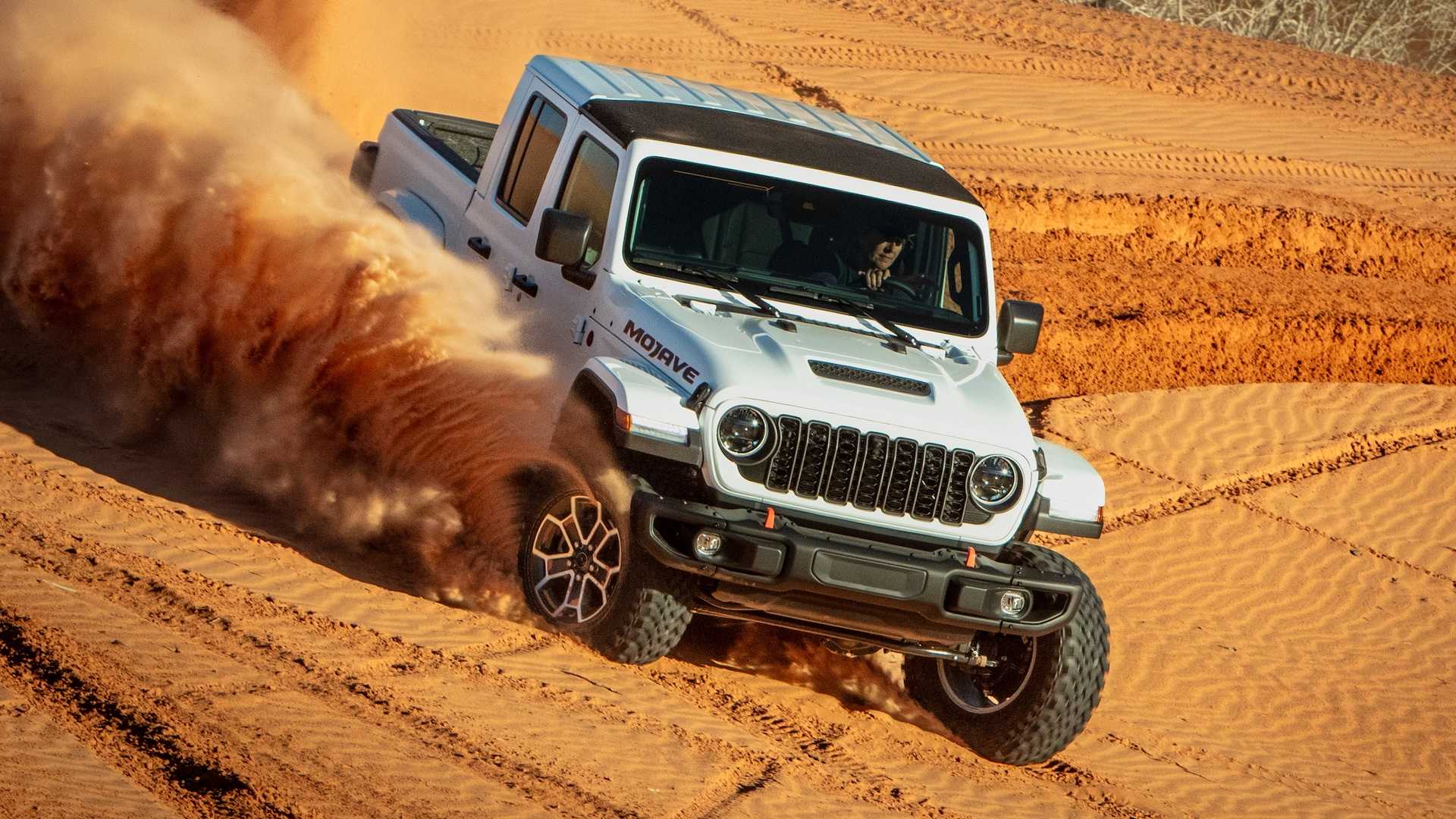 White Jeep Gladiator pickup truck throws up sand while skidding through the desert.