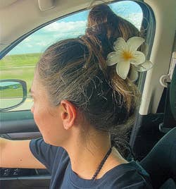 Person driving a car with a flower in their hair, wearing a casual T-shirt